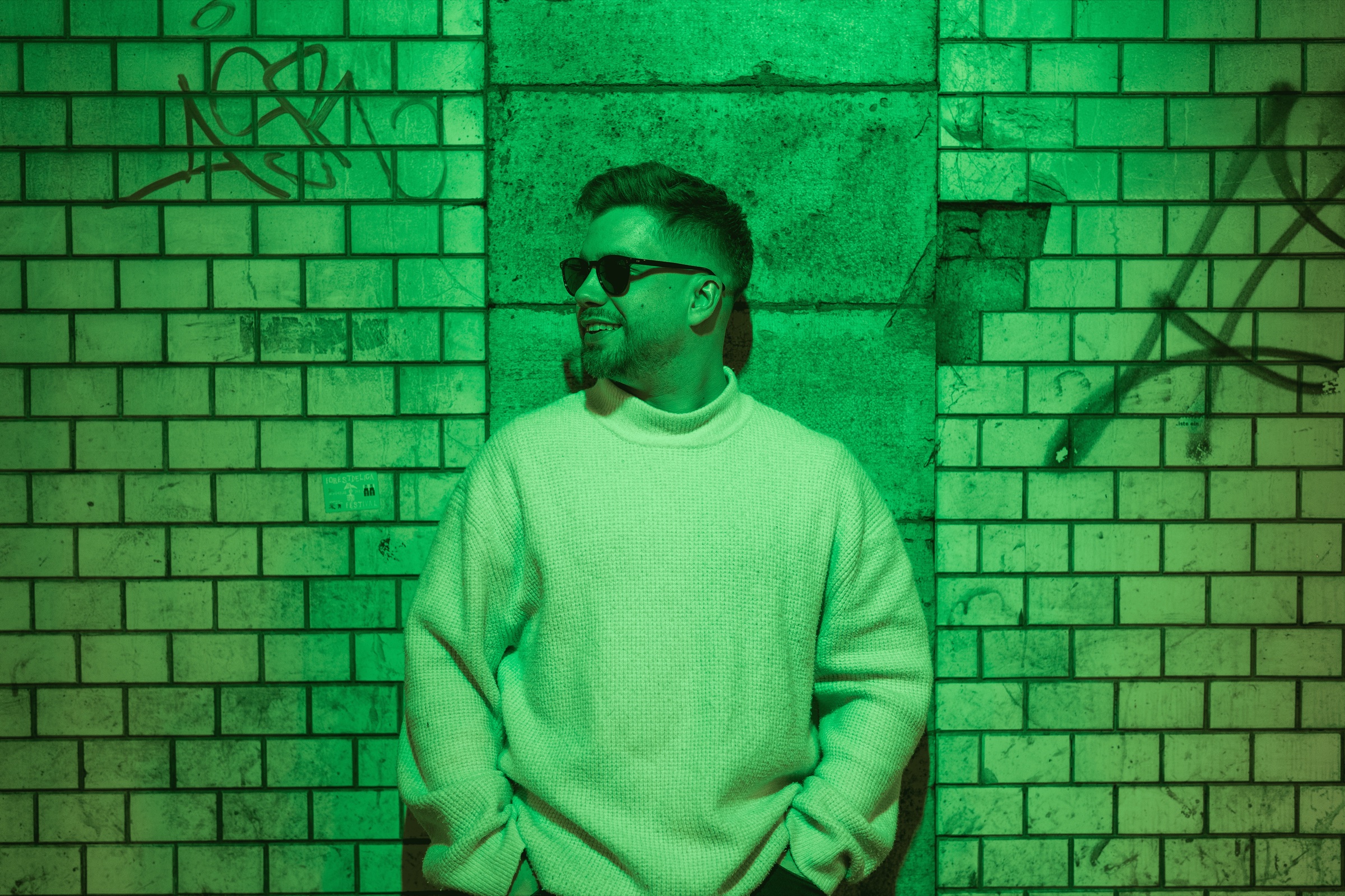 SIXLA posing with green neon lights and brick wall